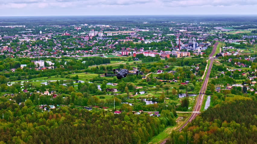 Aerial shot of a drone hovering over a landscape with green forests and a city.