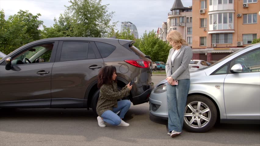 Upset African American woman taking photo of smashed vehicle on cellphone for insurance coverage, making evidence for pursuing claim against disappointed female driver after car accident on road.
