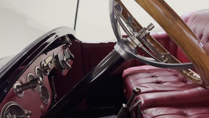 Close-up view of a vintage car interior featuring a polished wooden steering wheel, classic chrome details, and burgundy leather seats. 