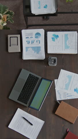 No people vertical shot of corporate employee desk in office, with laptop computer, business presentations, reports, contracts, notebook, focus zooming in on electronic device