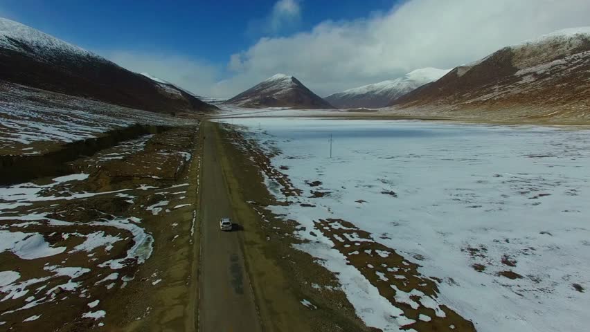 Car travels along a road through a snowy mountain landscape on a sunny day