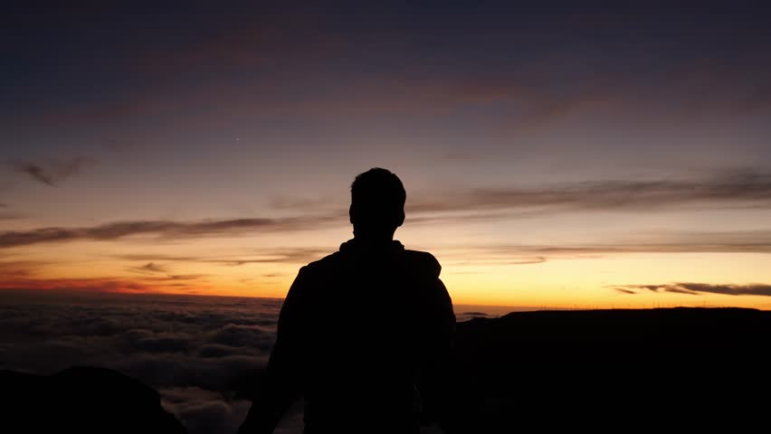 Silhouette of a man raising both arms in the air while watching the sunset at Pico do Arieiro, Madeira, Portugal.