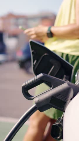 Woman charging electric car at public charging station