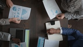 Top view of group of diverse business people in suits sitting around table at office meeting, examining data on financial report and shaking hands, congratulating on good performance results - Powered by Shutterstock - Get 15% off with code: PIKWIZARD15