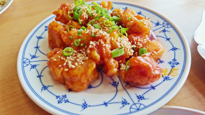 Traditional Chinese dish sweet and sour chicken. crispy fried chicken pieces coated in a glossy orange sauce, garnished fresh green onions sesame seeds. Chinese food. Authentic flavor Asian cuisine