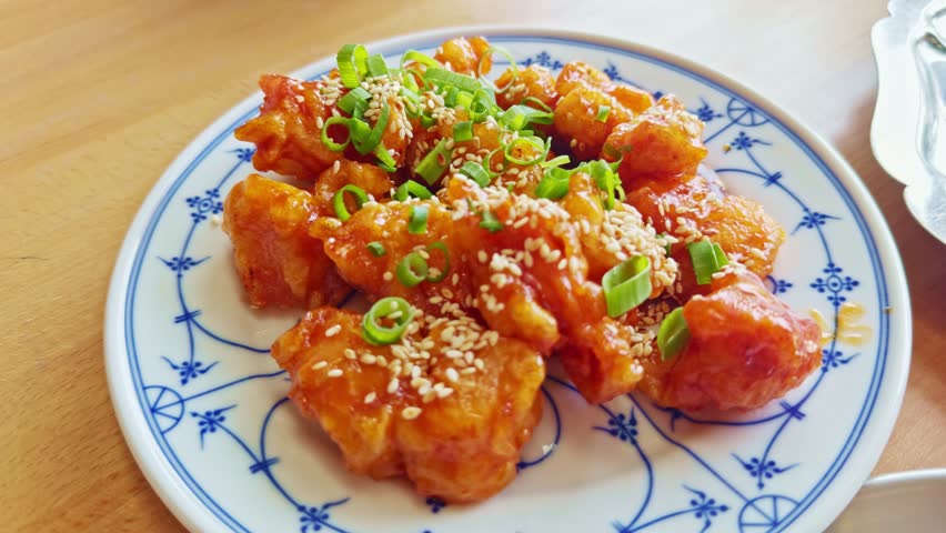 Traditional Chinese dish sweet and sour chicken. crispy fried chicken pieces coated in a glossy orange sauce, garnished fresh green onions sesame seeds. Chinese food. Authentic flavor Asian cuisine