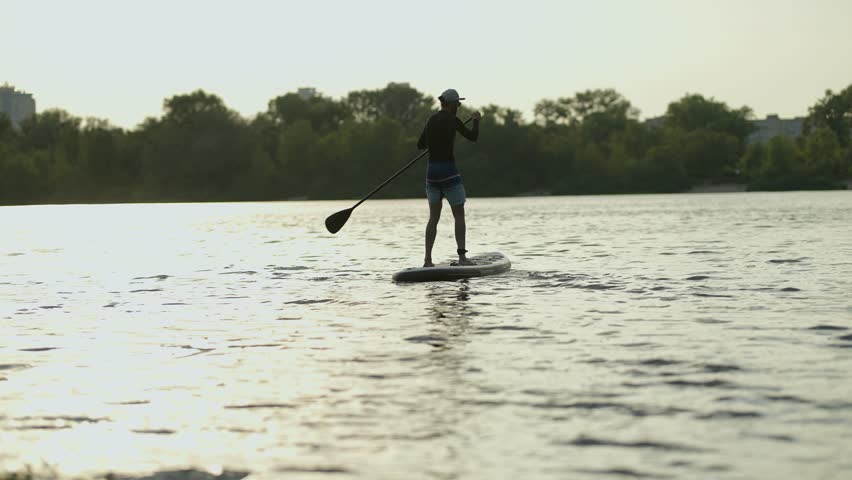 man floating on sup board. man enjoys paddleboarding on calm lake at sunset, silhouetted against serene water. Paddleboarder sup water sports, outdoor recreation, peace, and summer activities fun sup