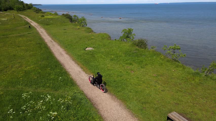 Aerial drone view flying behind a man riding his custom made black chopper bike with white wall fat tires on a Tabasalu cliff bank during a summer sunny day in Europe. Man is near steep cliff.