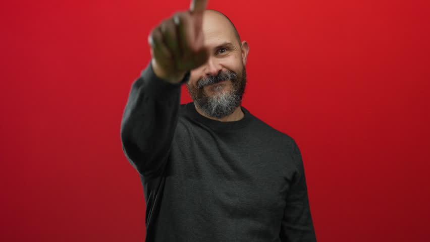 Bearded man gestures peace and points energetically against an isolated red background, creating an expressive and lively portrait.