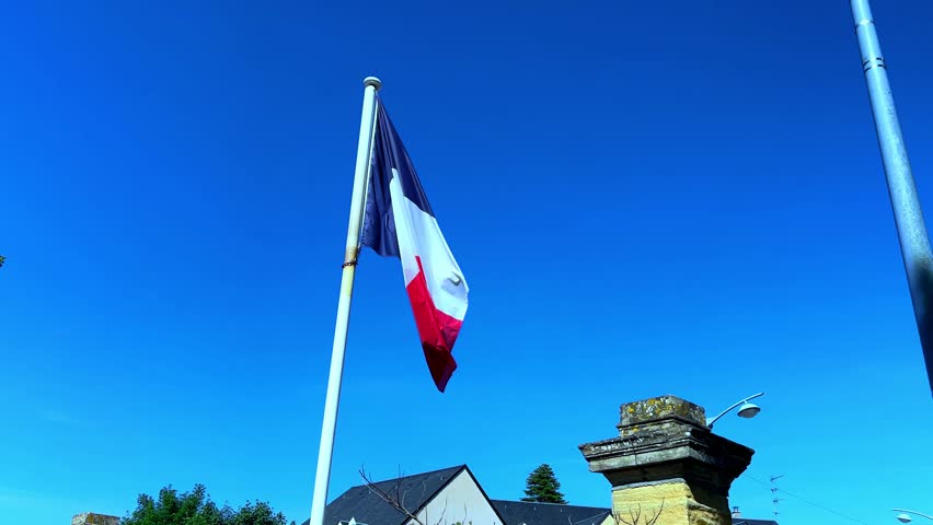 French flag slowly unfurling in the wind against a blue sky to show the full flag