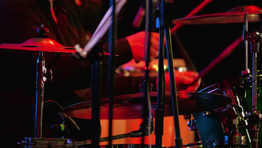 A drummer plays drums on a brightly lit stage. Close-up of the musician's virtuoso performance on the drum kit. Jazz or rock concert