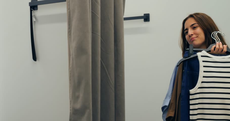 Woman trying denim clothes and striped shirt in dressing room, woman exploring denim styling options and outfit variations, scene perfect for casual fashion campaigns and social media reels