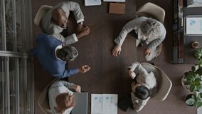 Top view of five multiethnic male and female corporate employees in suits and director sitting around table during team building meeting, joining hands in middle to boost morale - Powered by Shutterstock - Get 15% off with code: PIKWIZARD15