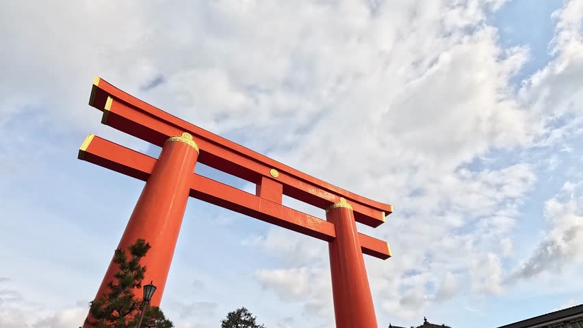 Looking Up at Massive Vermilion Torii Gate with Gold Accents Under Cloudy Sky at Heian Shrine Entrance in Kyoto, Japan