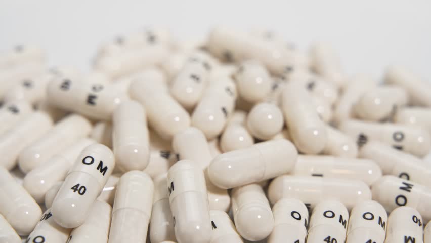 Capsule Macro Rotation. Close-up rotating shot of many identical capsules highlights text and capsule ends. Texture and light reflections are emphasized.