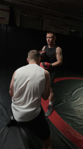 Vertical shot of professional male boxer delivering sharp punches at focus mitts held by trainer while having intense ring session