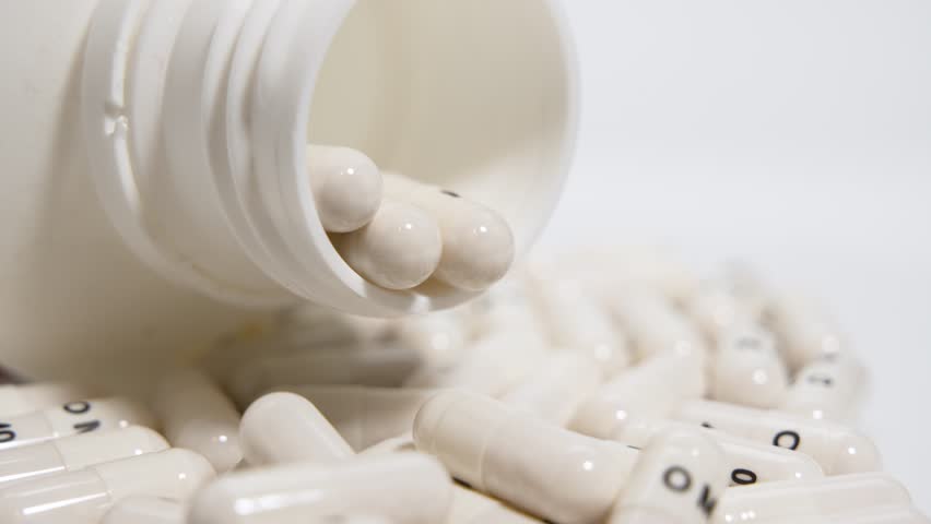 Capsules Pouring from Bottle. A container tips slowly while capsules pour out in a rotating motion. Focus is on the transition from bottle to surface.