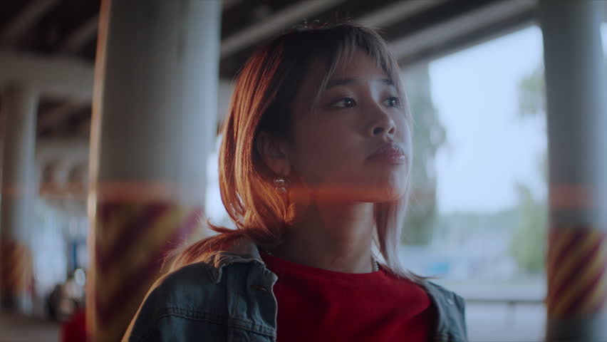 Pretty young Asian woman with short hair under overpass bridge at sunset light. Quiet female stands alone at empty parking site in modern urban district