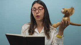 Young hispanic woman reading aloud from book holding toy lion against blue background wall wearing glasses and watch - Powered by Shutterstock - Get 15% off with code: PIKWIZARD15