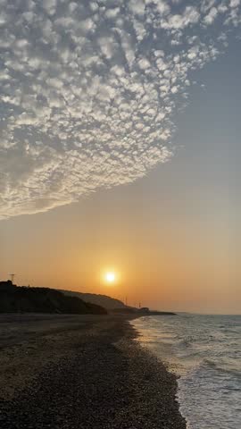Wide view of a sunset over the sea with textured clouds and a gentle shoreline.