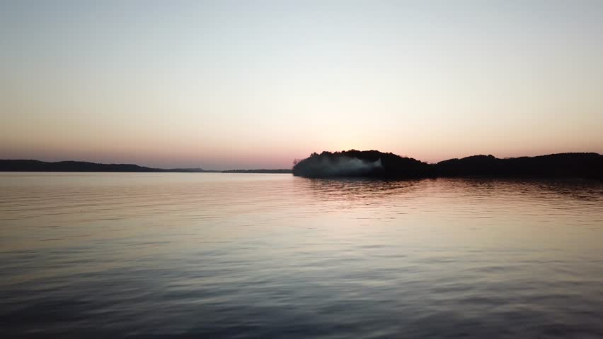 A calm Lake Wisconsin reflects the pastel tones of twilight as smoke drifts from a wooded peninsula. This wide aerial view captures serene beauty and atmospheric light in a peaceful dusk setting.