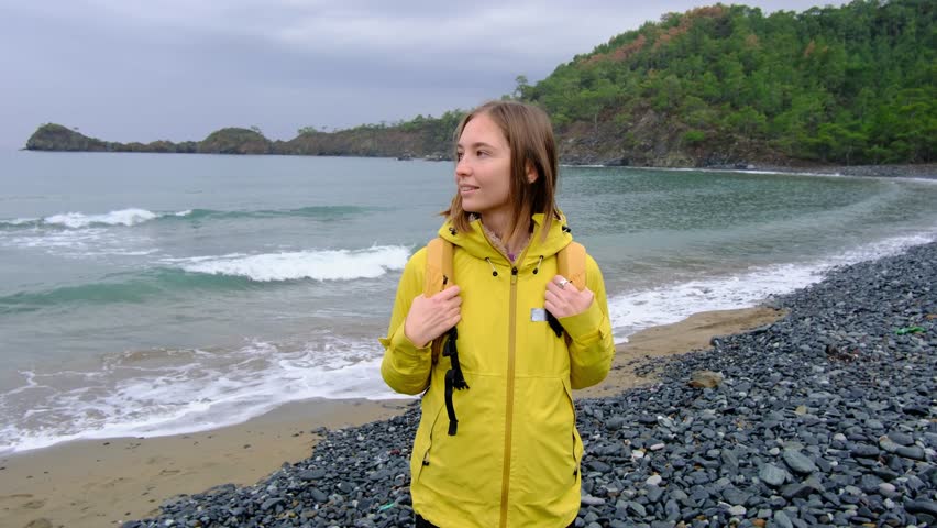 Young woman walks alone along cold Turkish coast. Windy, cloudy weather, peaceful solitude and gentle connection with nature by stormy sea.