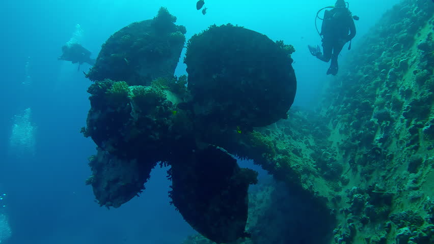 Propeller of the wreck ferry Salem Express in backlit, scuba divers look at it, Slow motion, Camera moving forwards approaching the propeller of the sunken ship on blue water background