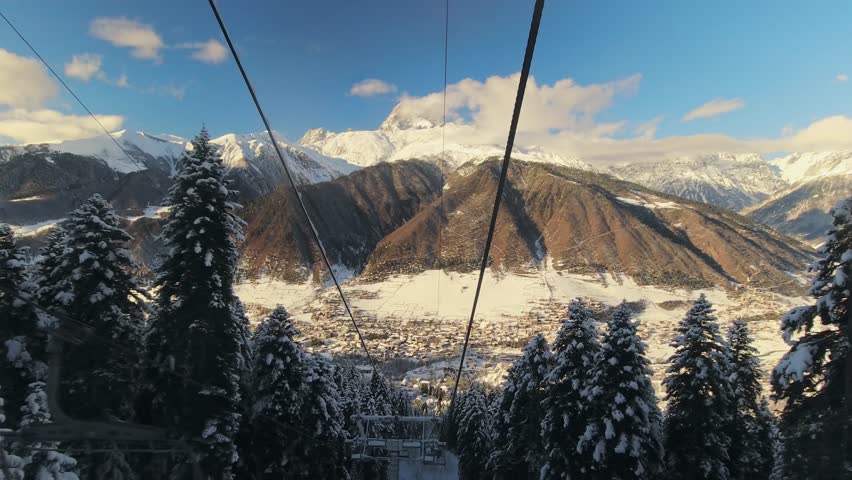Ski lift descending through snowy forest revealing panoramic view of Mestia town and Caucasus mountains in winter Svaneti Georgia.Hatsvali skiing winter landscape outdoors concept