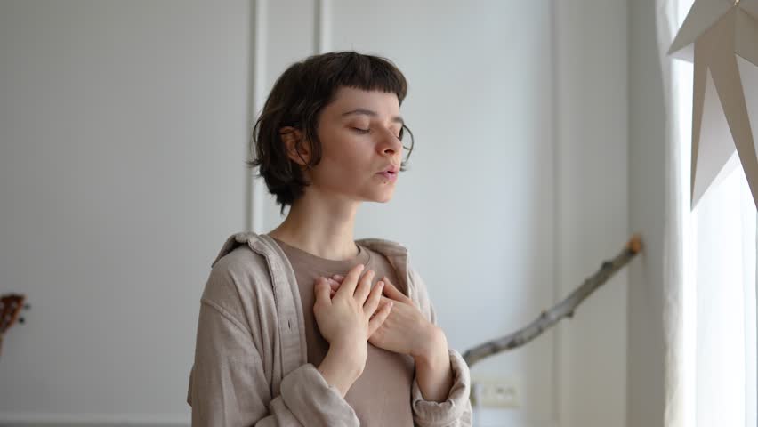 Relaxed young woman breathing deeply with hands resting on chest, turning inward for reflection. Meditation practice, zen spiritual connection, mindfulness routine, emotional balance, inner peace