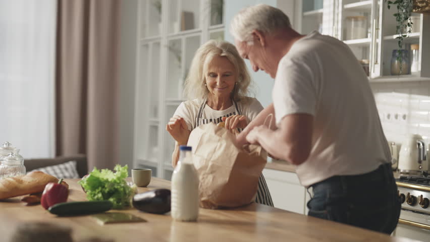 Calm and happy sunday morning in kitchen, joyful old spouses unpacking eco bag. Healthy nutrition and diet for stay active in old age, low-calories and tasty food from eco farm, food delivery service