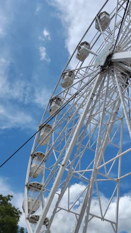 Daytime view from the base of a ferris wheel at a festive fair. Bright sky, joyful atmosphere, people enjoying the ride. Perfect for travel, fun, and carefree vibes