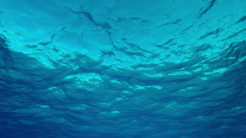 Natural background with ripples on blue surface of water, Underwater view of sea waves, Slow motion of waves on turquoise surface of Ocean, Undersea scene below water surface