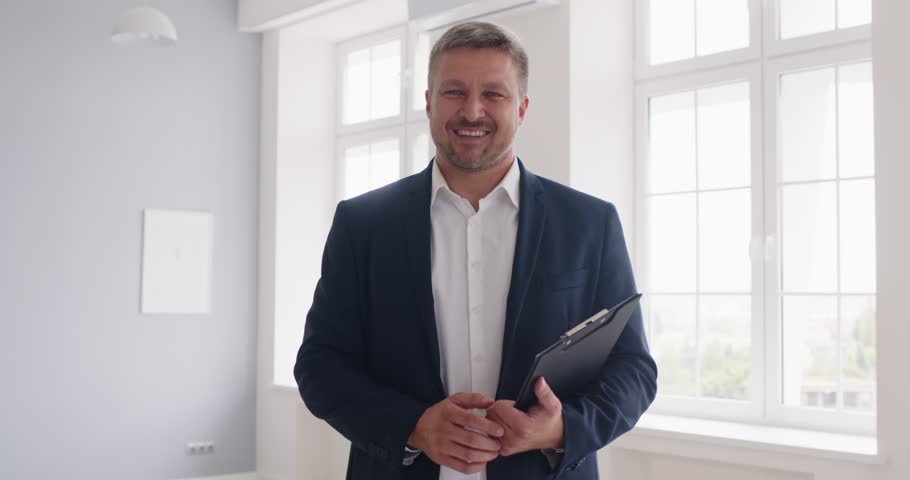 Welcome, happy smiling mature professional male realtor, agent broker holding paper agreement, showing, proposing renovated news stylish apartment to client, real estate service, advertisement estate