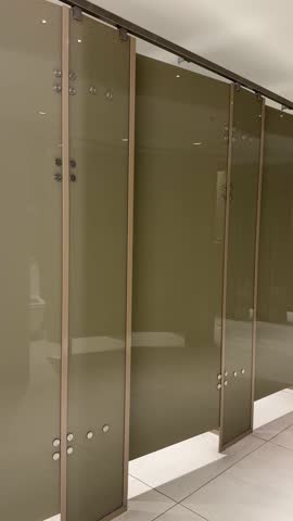 Contemporary public restroom interior featuring sleek frosted glass partition doors, clean tiled flooring, modern architectural 4k footage. public toilet or restroom. Row of opened doors. vertical