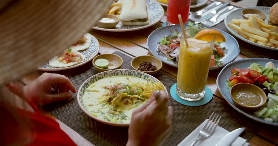 Person enjoying Mexican cuisine in outdoor restaurant. Dishes include tacos, salad, curry. Vibrant drinks complement colorful meal. Dining concept, casual atmosphere, summer vibes.