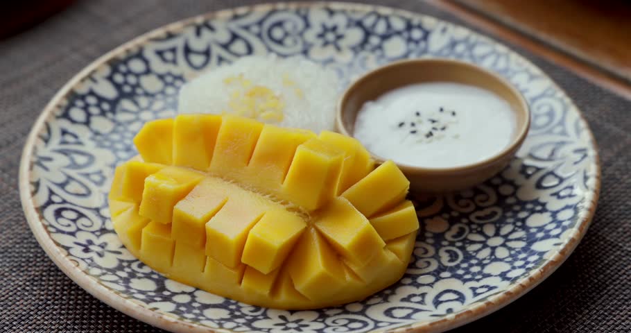 Mango sticky rice dessert on patterned plate, traditional Thai cuisine with ripe mango slices, sweet coconut milk, and sticky rice, exotic Asian Thailand flavor.