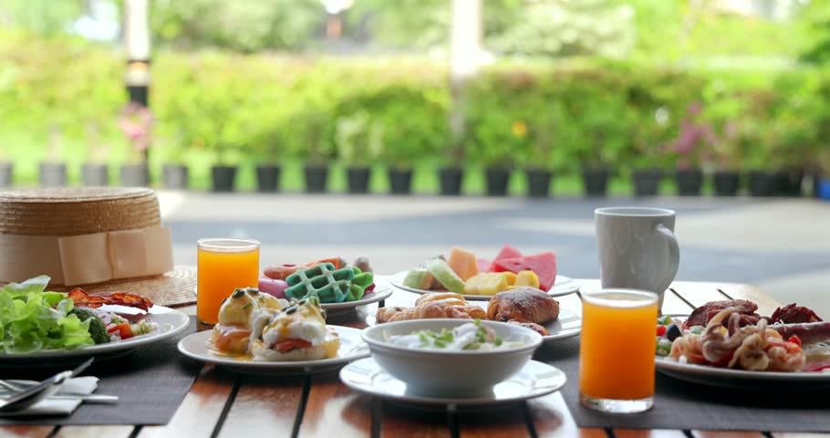 Outdoor breakfast spread on wooden table with fresh fruits, pastries, juice, coffee, and salad. Morning sunlight. Garden view. Relaxation, dining, healthy lifestyle concept.