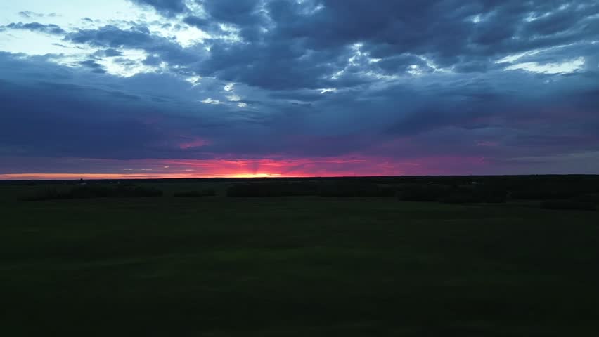 red sunrise with pink purple sky over the horizon, drone footage in the fields