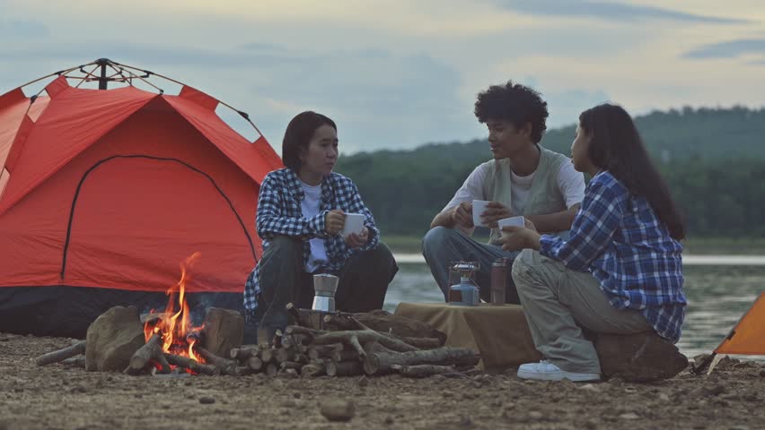 Group of friends enjoying coffee in natural campsite, warm morning gathering by the fire with moka pot, cozy camping breakfast with hot coffee and friendship.