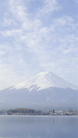 Mount Fuji rises majestically above the landscape, its snow-covered peak gleaming under a bright blue sky. Kawaguchi Lake, Japan. Vertical video