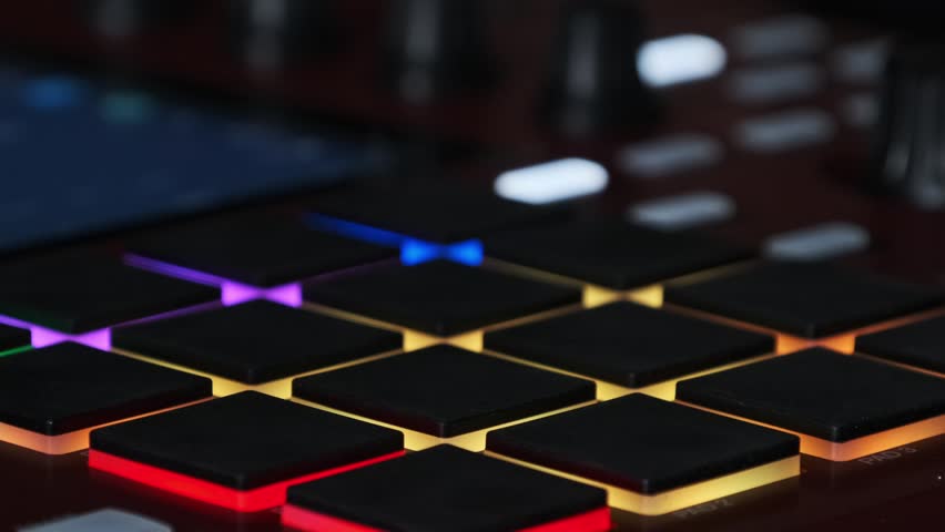 Macro close-up of a producer's fingers rapidly tapping a rhythm on the glowing pads of a beat machine. The electronic drum pads flash with red and orange light during a fast-paced music session.