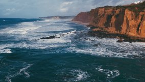 The breathtaking coastal scenery showcases the powerful ocean waves that crash with immense force against the rugged cliffs, all beneath a dramatically beautiful sky filled with clouds and sunlight - Powered by Shutterstock - Get 15% off with code: PIKWIZARD15