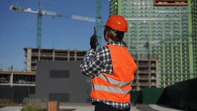 A safe ty clad construction worker is communicating effectively at a busy building site with cranes in the background - Powered by Shutterstock - Get 15% off with code: PIKWIZARD15