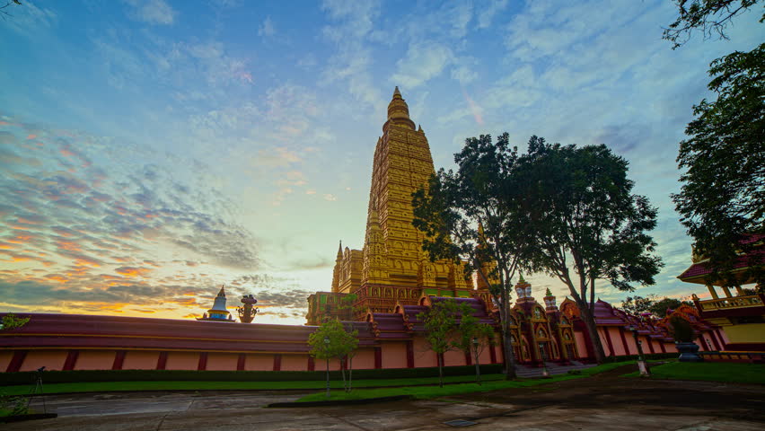 Time lapse A stunning golden pagoda stands majestically under a vibrant morning sky, surrounded by traditional temple architecture. The warm sunlight casts a serene glow, enhancing the spiritual