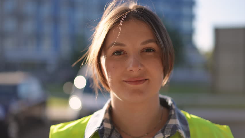A confident young woman in safety gear smiling at a construction site, showcasing empowerment and professionalism.