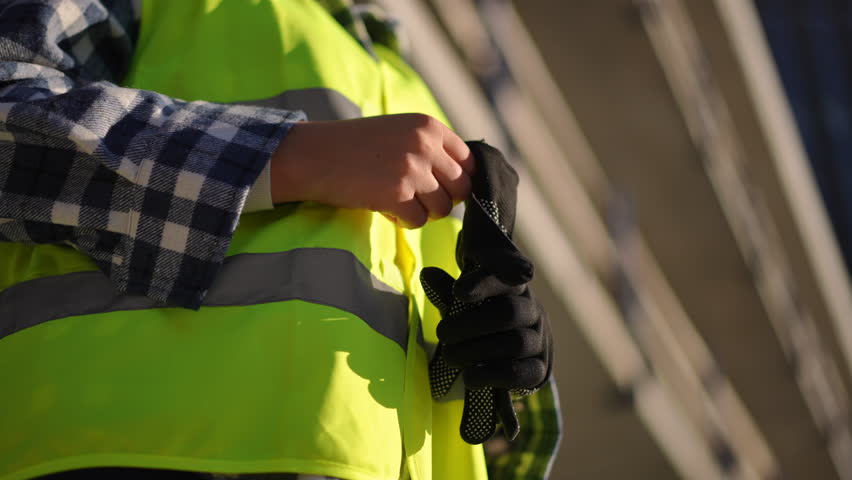 A diligent worker is putting on gloves while wearing a bright safety vest, getting ready for their job site