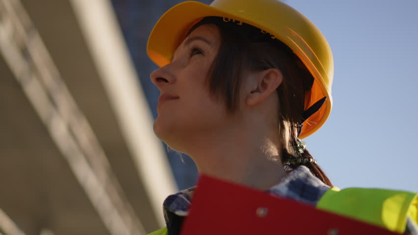 A confident construction worker, wearing essential safety gear, gazes towards the bright blue sky on a sunny day