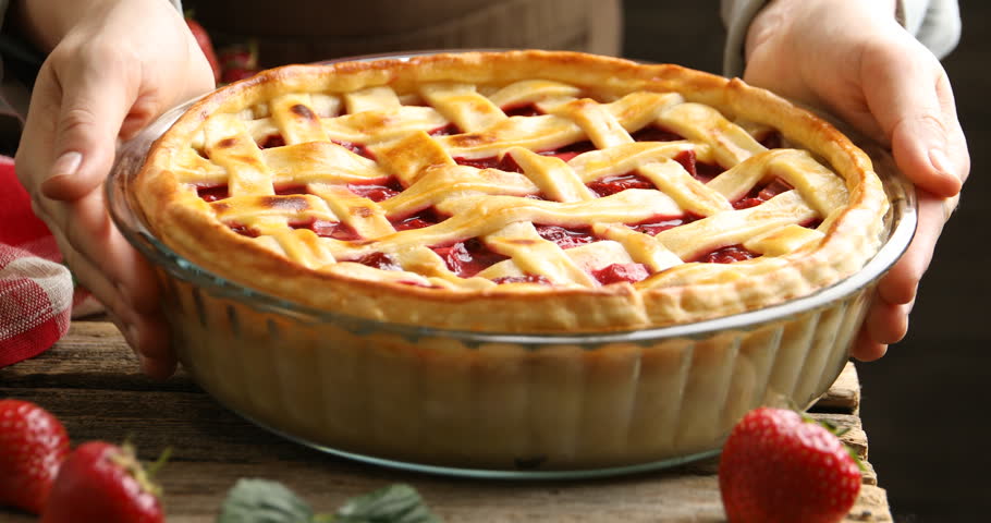 Woman putting tasty strawberry pie at wooden table, closeup