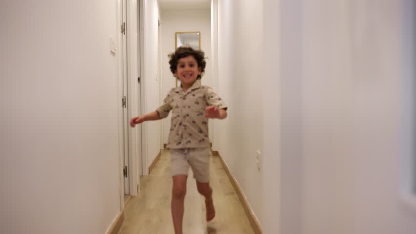 Young boy running with infectious joy along white-walled corridor, showcasing playful childhood energy and carefree happiness in family home interior