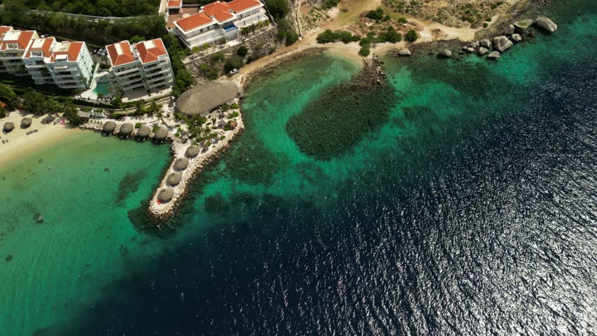 Daylight shot of Blue Bay with umbrellas, hotels nearby, and calm waves. Ideal for summer getaway promos and island tourism.